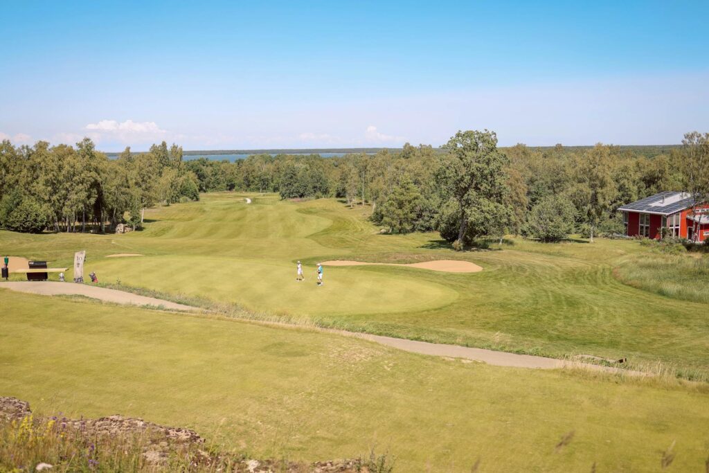 A scenic shot of a golf course under the sun with players in action, illustrating the importance to stay hydrated golfing heat.