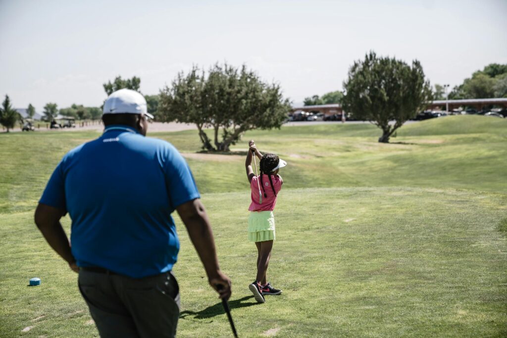 An adult helping a child with their swing on a golf course, illustrating mentorship. — golf courses for families