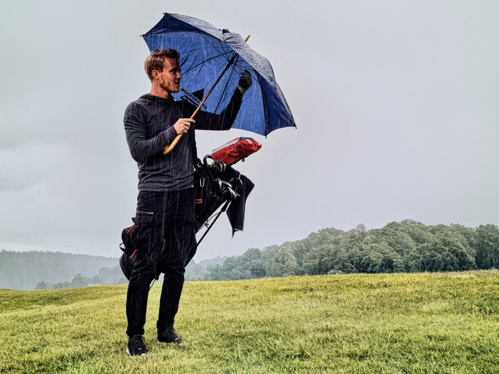 A golfer using a rain umbrella while playing a shot — weather effects on Dungeness golf